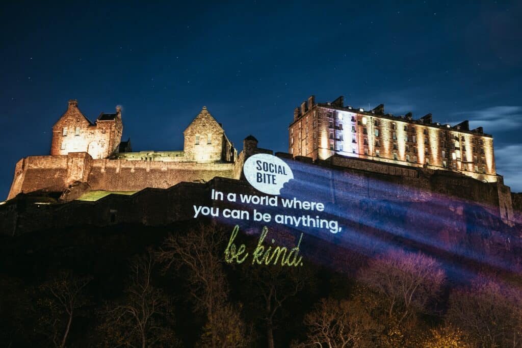 Edinburgh castle lit up at night with Social Bite logo shone onto the side of the castle