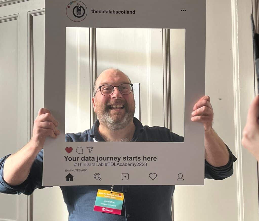 glasgow university lecturer holding an carboard instagram frame and smiling through it