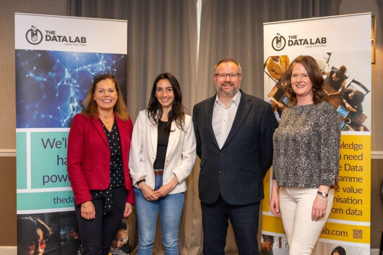 A group of people standing next to each other in front of The Data Lab signage. From left to right Emma Walker (Auticon), Sara Votta (The Data Shed), Brian Hills (The Data Lab), Sandra Ripley (The Data Lab)